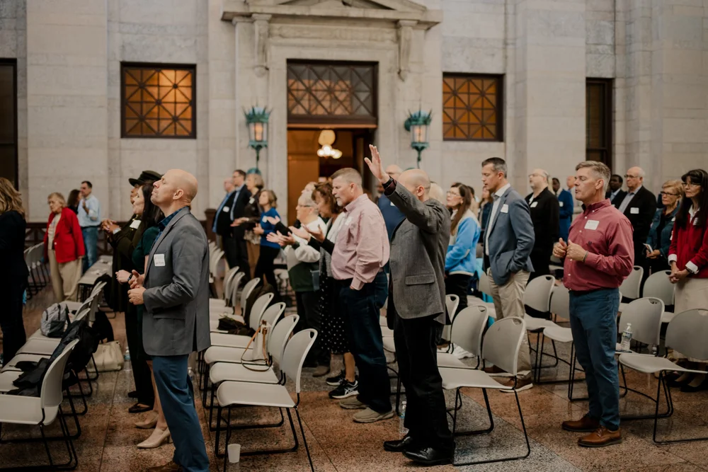 Standing among the chairs, a hand raised